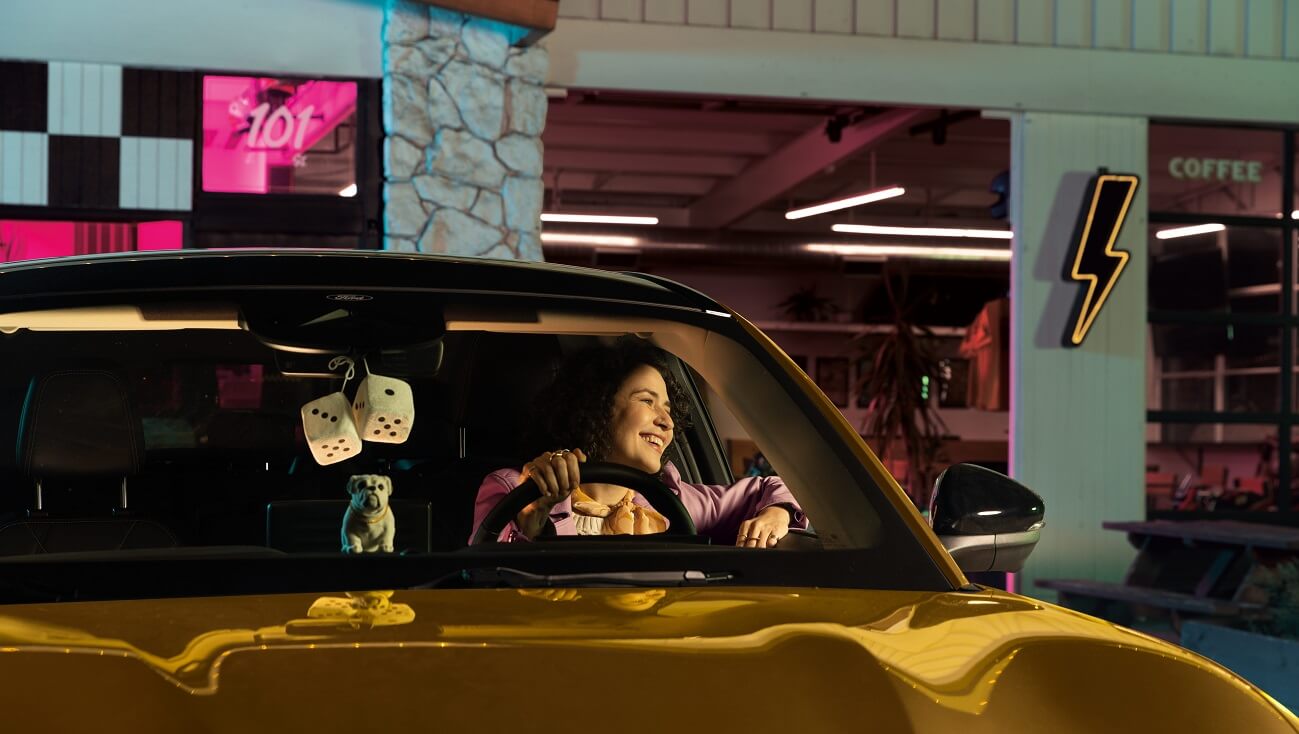 A woman sitting and smiling at the driver's seat of her electric Ford Mustang.