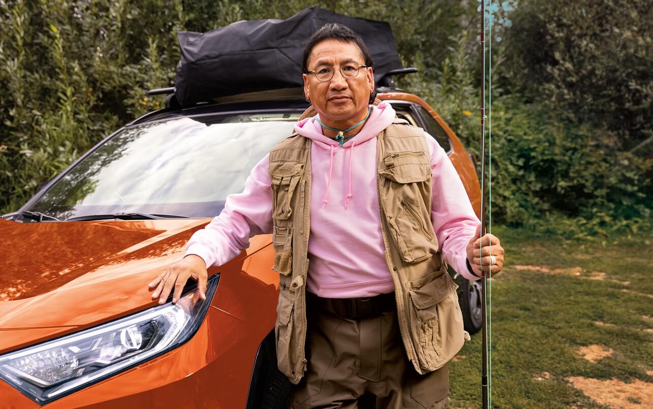 A man with a fishing pole posing for a photo in front of his electric vehicle.