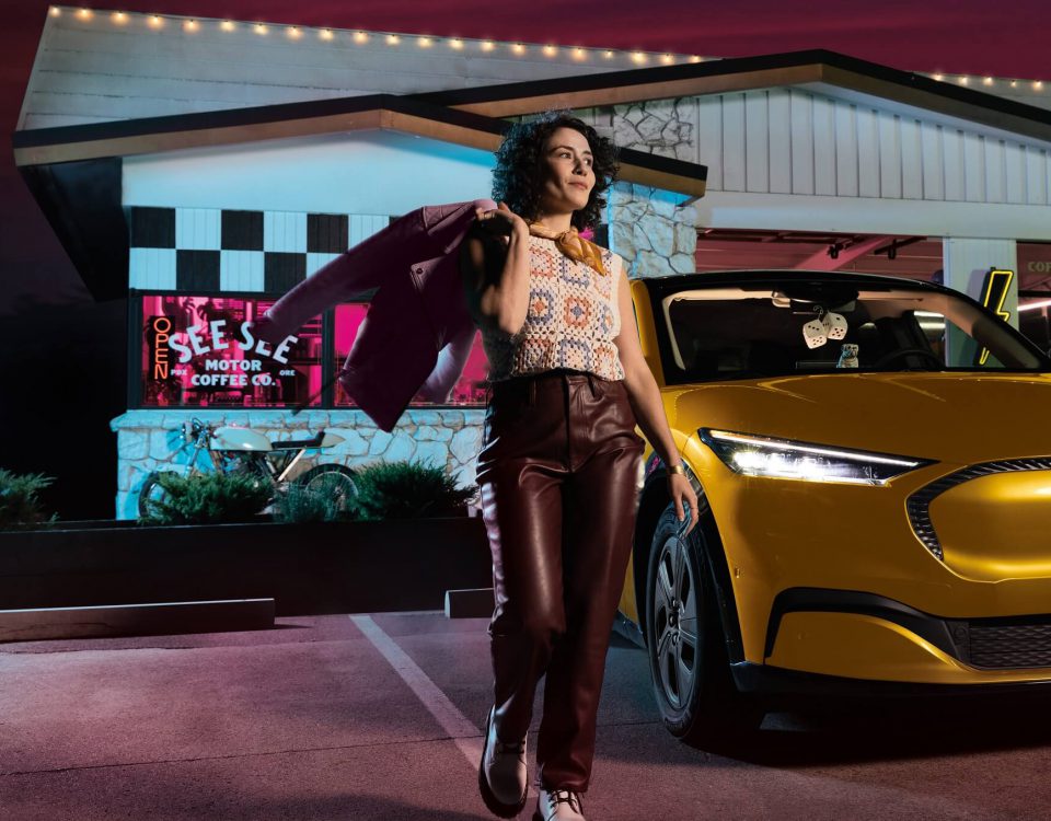 A woman standing in front of her gold electric Ford Mustang.