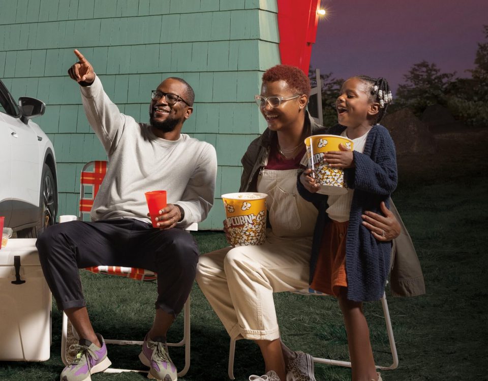 A mom, dad, and two young kids having fun at a drive-in movie theater.